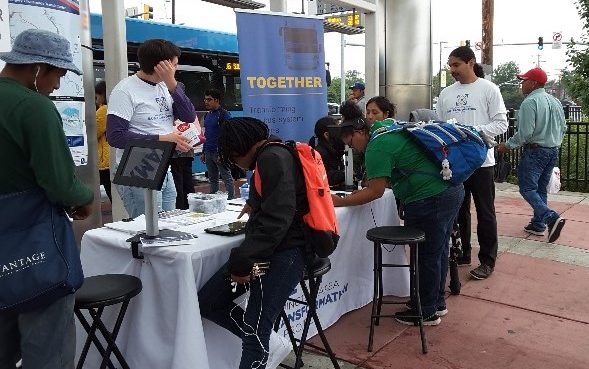 This picture shows people filling out surveys via tablets at a pop-up event outside of a bus station.